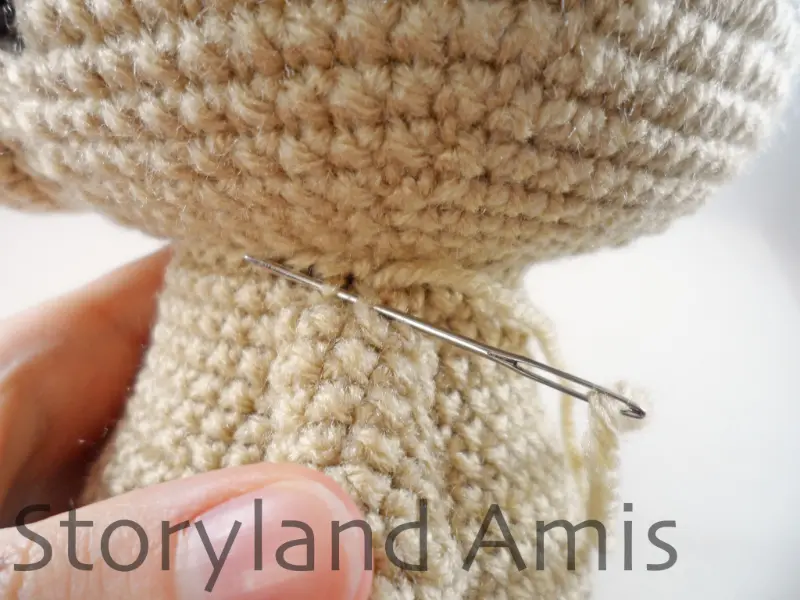 A close-up of a tapestry needle being used to sew a crocheted arm to the side of an amigurumi puppy dog.