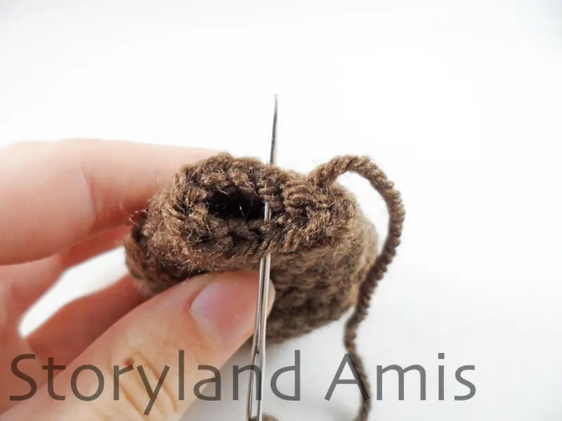 A hand uses a tapestry needle to sew the opening closed on a crocheted dog ear.