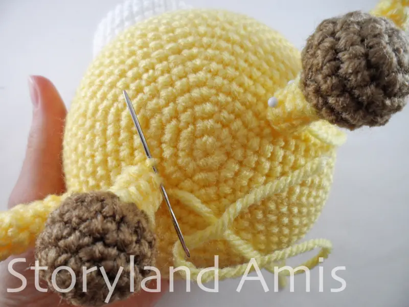 A close-up of a crocheted yellow and brown horn being sewn to the head of an amigurumi giraffe using a tapestry needle.