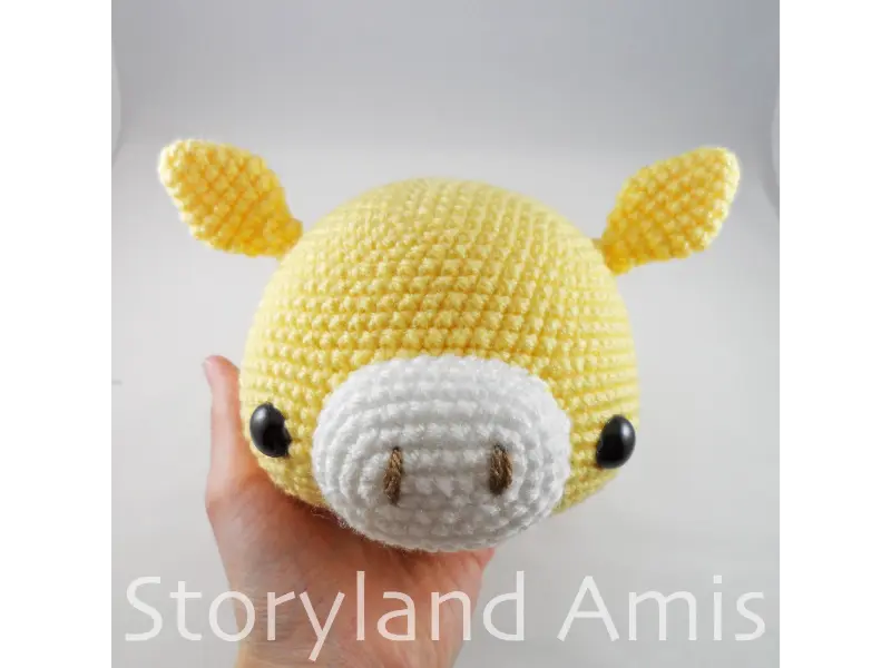 A hand holds up a crocheted amigurumi giraffe head.