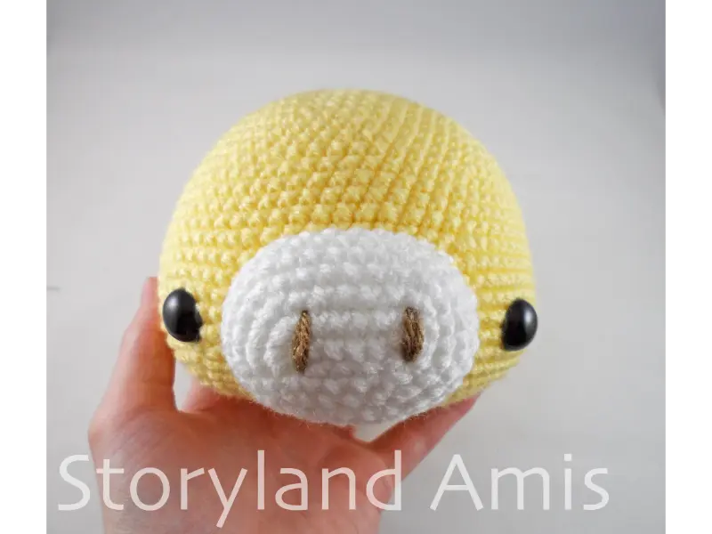 A hand holds up a partially made yellow, crocheted giraffe head.