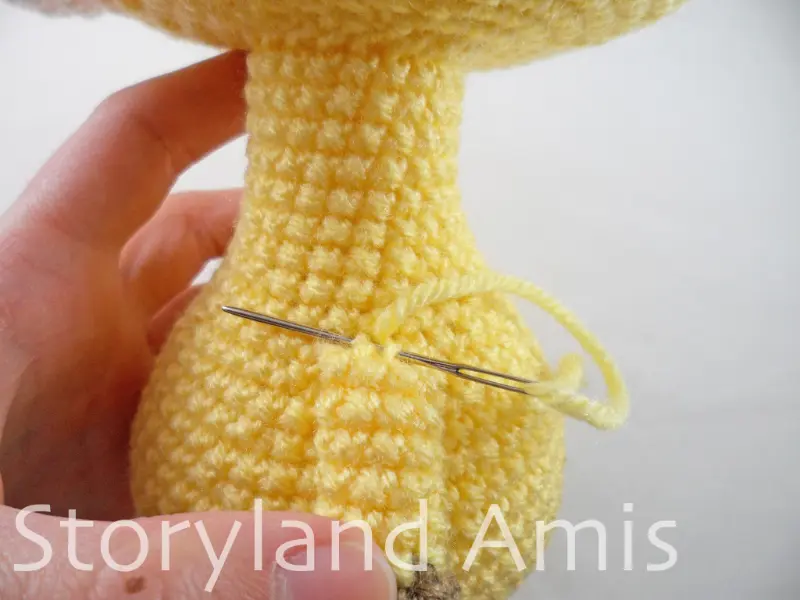 A close-up of a hand using a silver tapestry needle to sew a crocheted arm to an amigurumi giraffe's body.