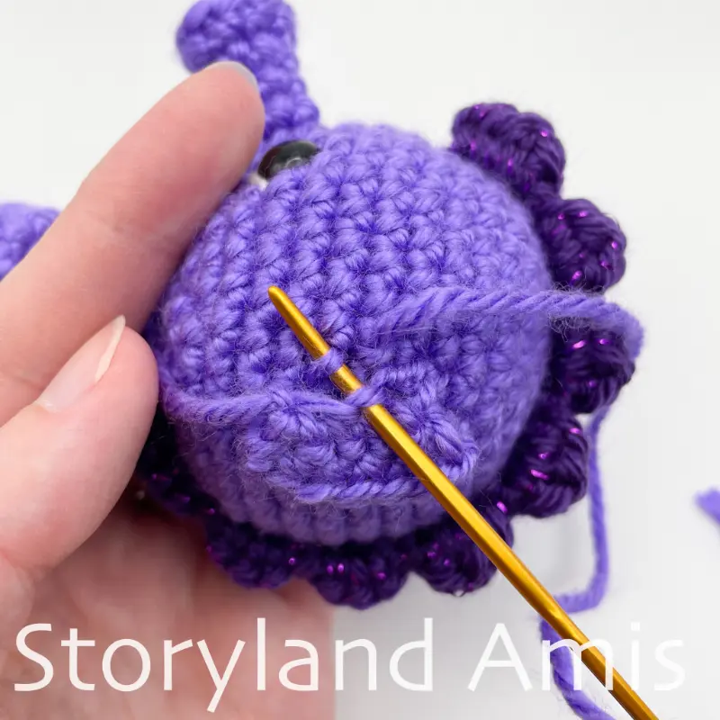 A close-up of a tapestry needle being used to sew a crocheted fin to the side of an amigurumi seahorse's head.