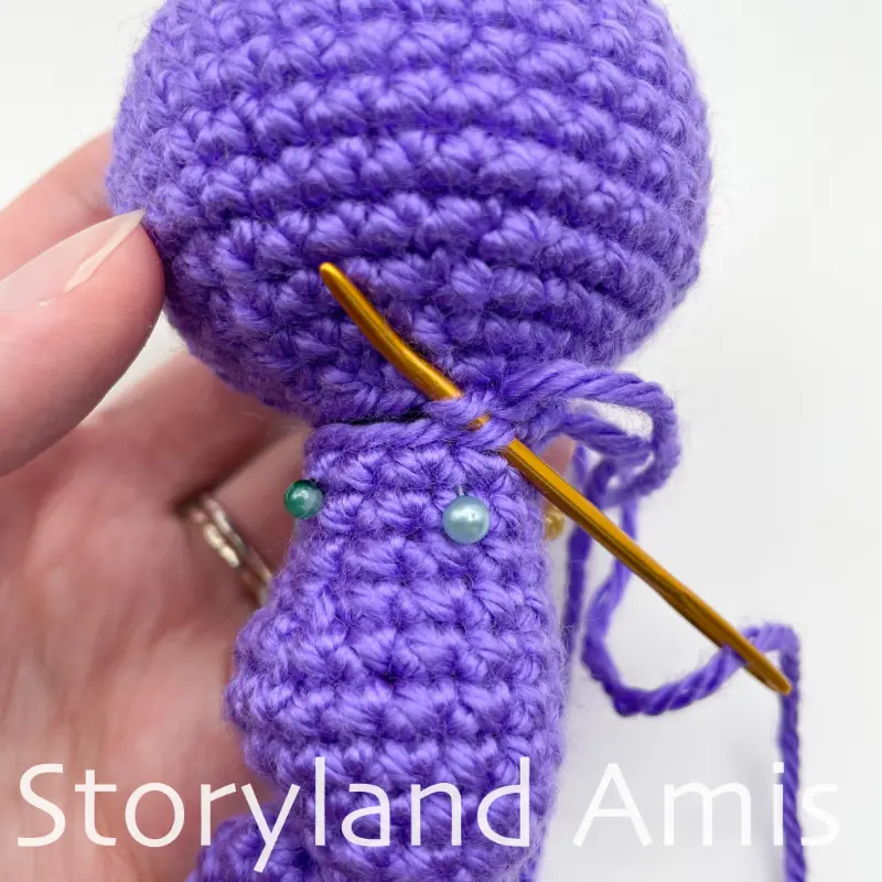 A gold tapestry needle is used to sew a purple crocheted body to an amigurumi seahorse's head.
