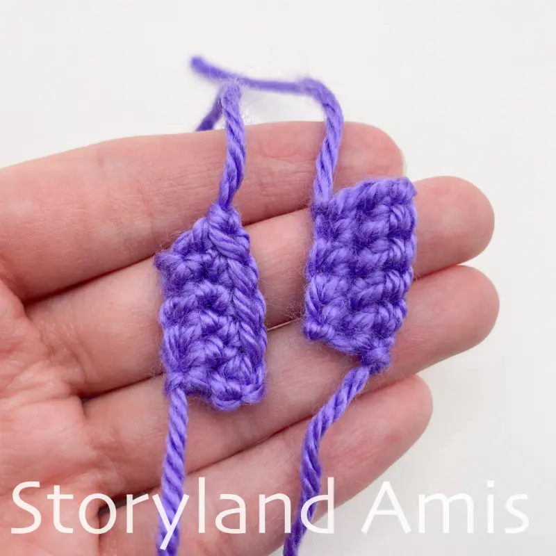 A hand holds two small purple crocheted rectangles.