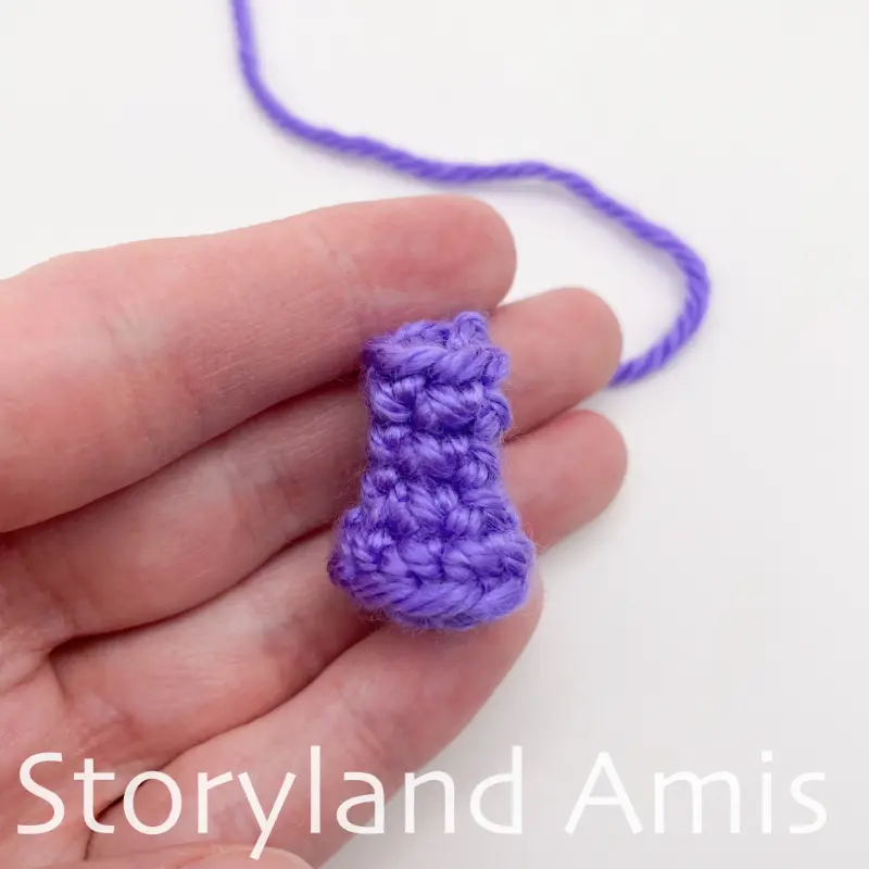 A hand holds a small crocheted purple snout for an amigurumi seahorse.