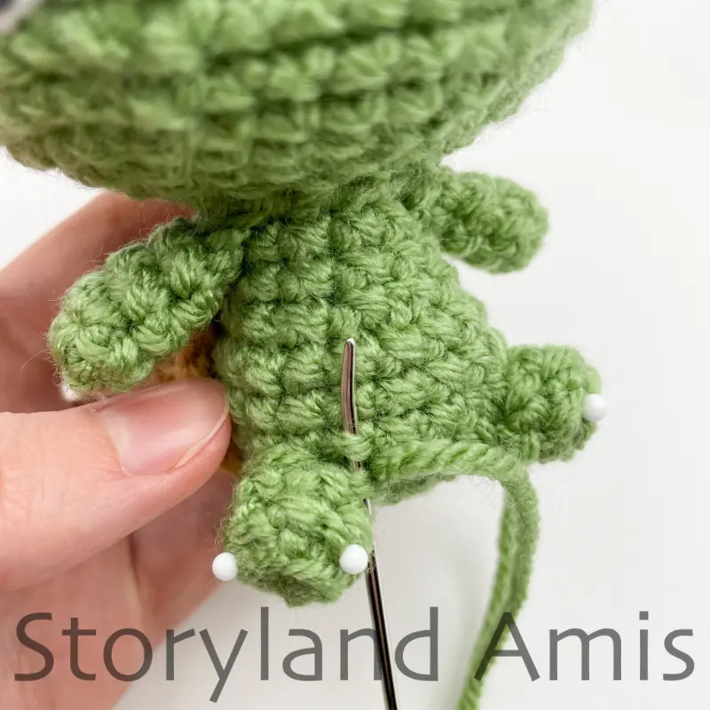 A close-up of a tapestry needle being used to sew a small leg to the body of an amigurumi tortoise.