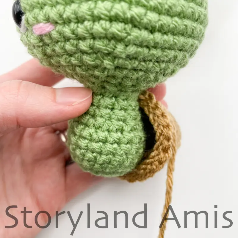 A close-up of an amigurumi tortoise's body with the shell sewn partially on.