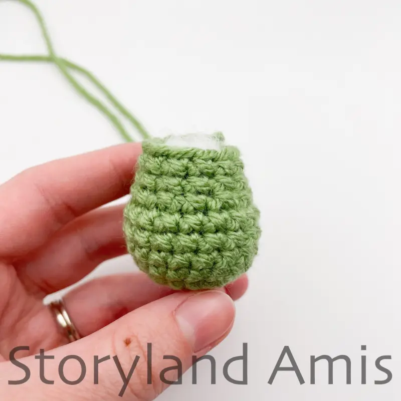 A hand holds a small green, crocheted body for an amigurumi tortoise.