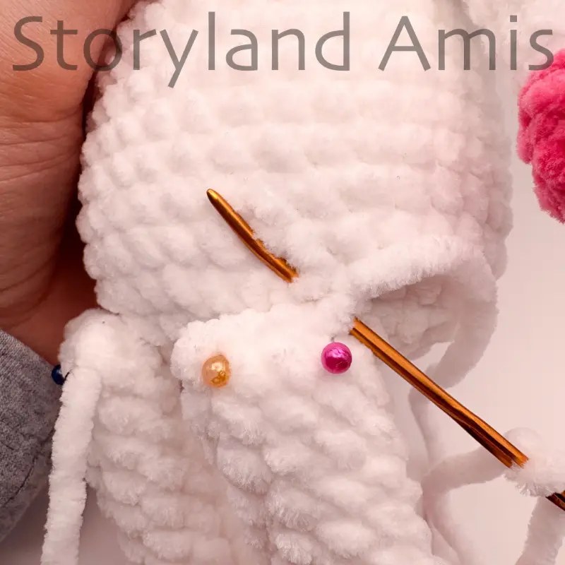 A close-up of a tapestry needle being used to sew a crocheted leg to the body of an amigurumi unicorn. 
