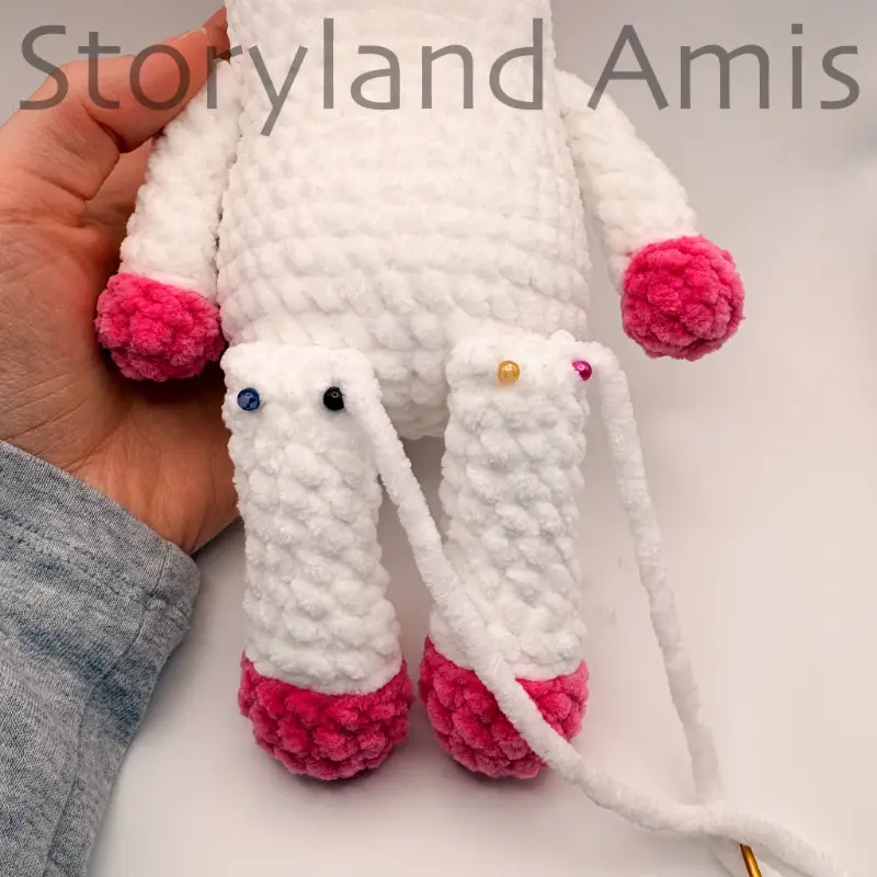A close-up of an amigurumi unicorn's body with the legs pinned to the body with straight pins.