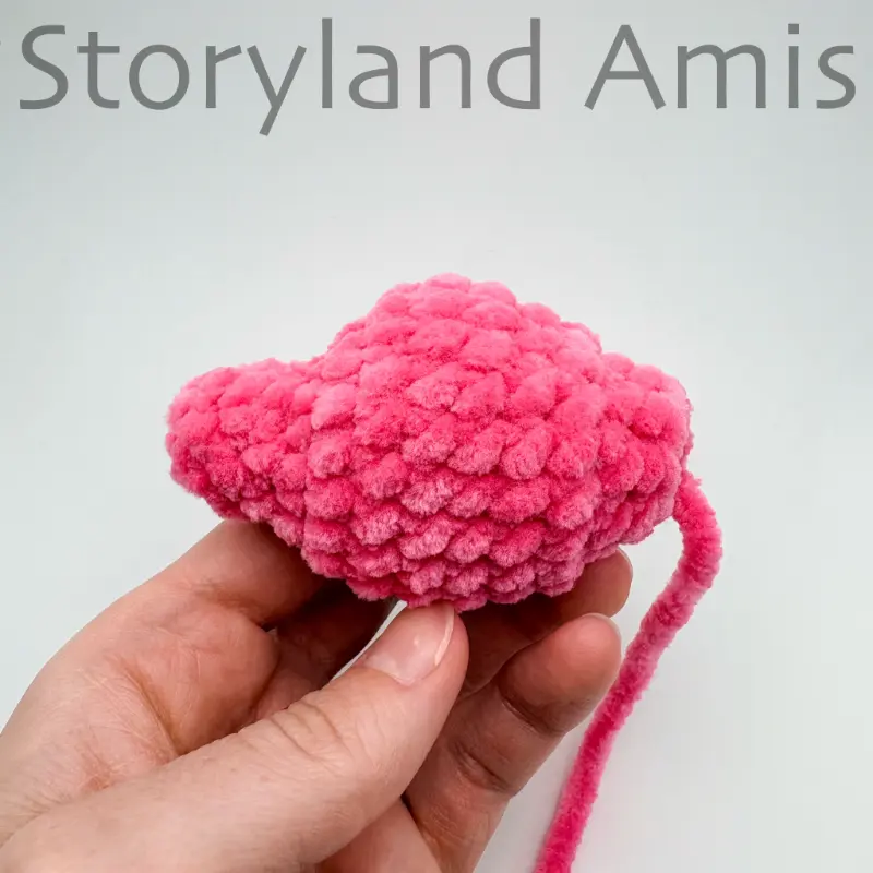 A hand holds up a pink crocheted unicorn tail.