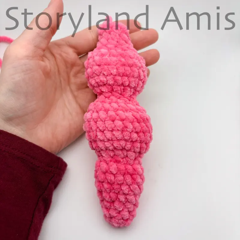 A hand holds a pink crocheted unicorn mane.