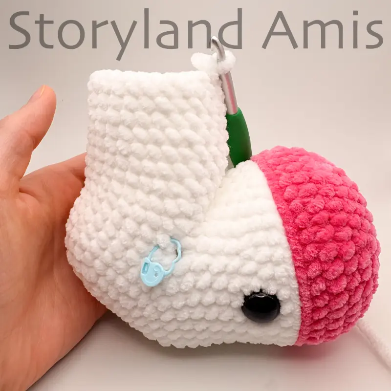 A hand steadies a partially crocheted amigurumi unicorn. A green crochet hook is inserted in a stitch of the body.