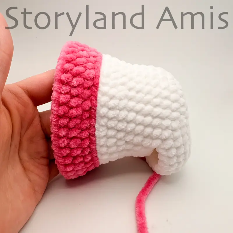 A hand steadies a partially crocheted amigurumi unicorn head.