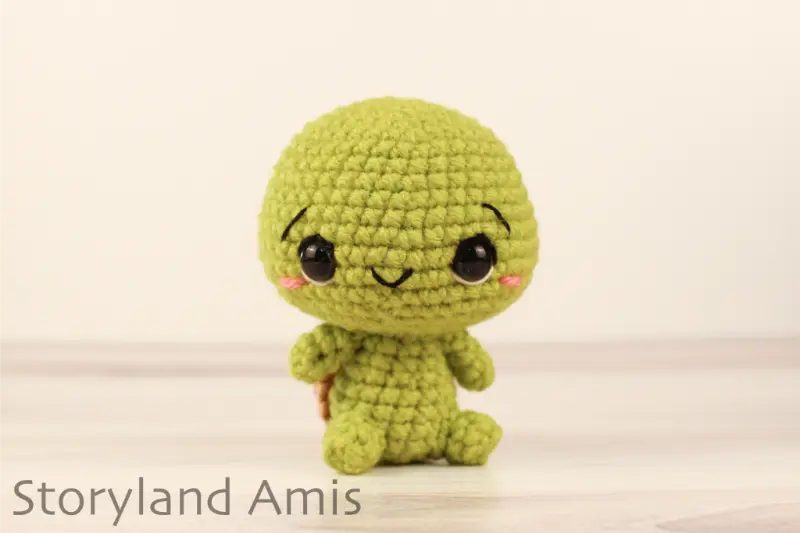 A crocheted amigurumi tortoise sits on a wooden table against a white backdrop.
