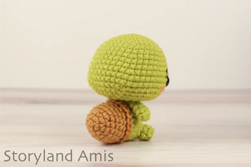 A crocheted amigurumi tortoise sits on a wooden table against a white backdrop.