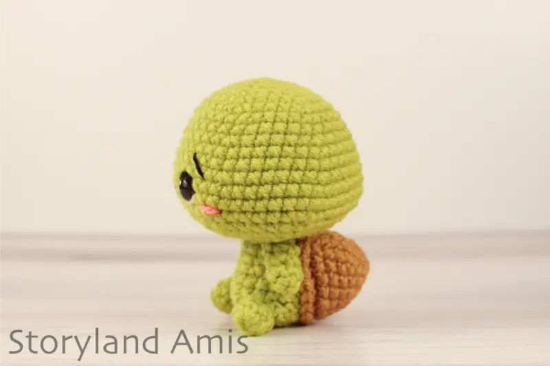 A crocheted amigurumi tortoise sits on a wooden table against a white backdrop.