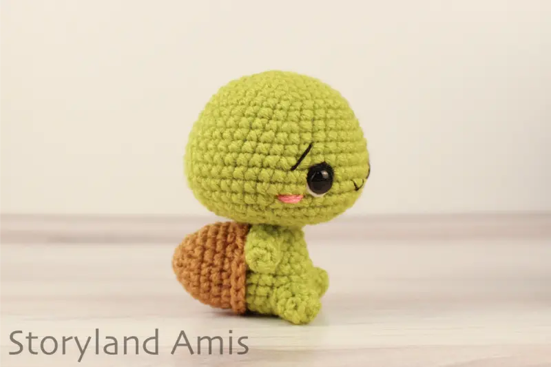 A crocheted amigurumi tortoise sits on a wooden table against a white backdrop.