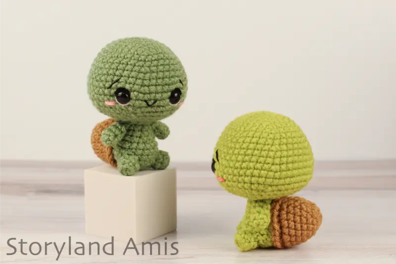 Two amigurumi tortoises sit on a wooden table.