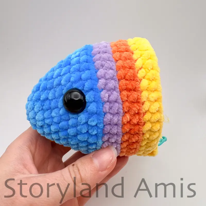 A hand holds a partially finished crocheted fish.