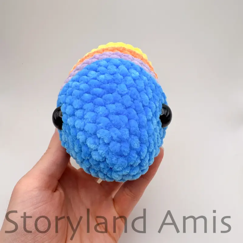 A hand holds a partially finished crocheted fish.