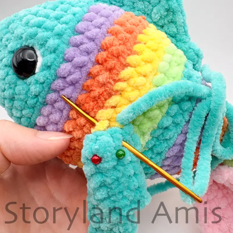 A close-up shows a tapestry needle being used to sew a crocheted fin to the body of an amigurumi fish.