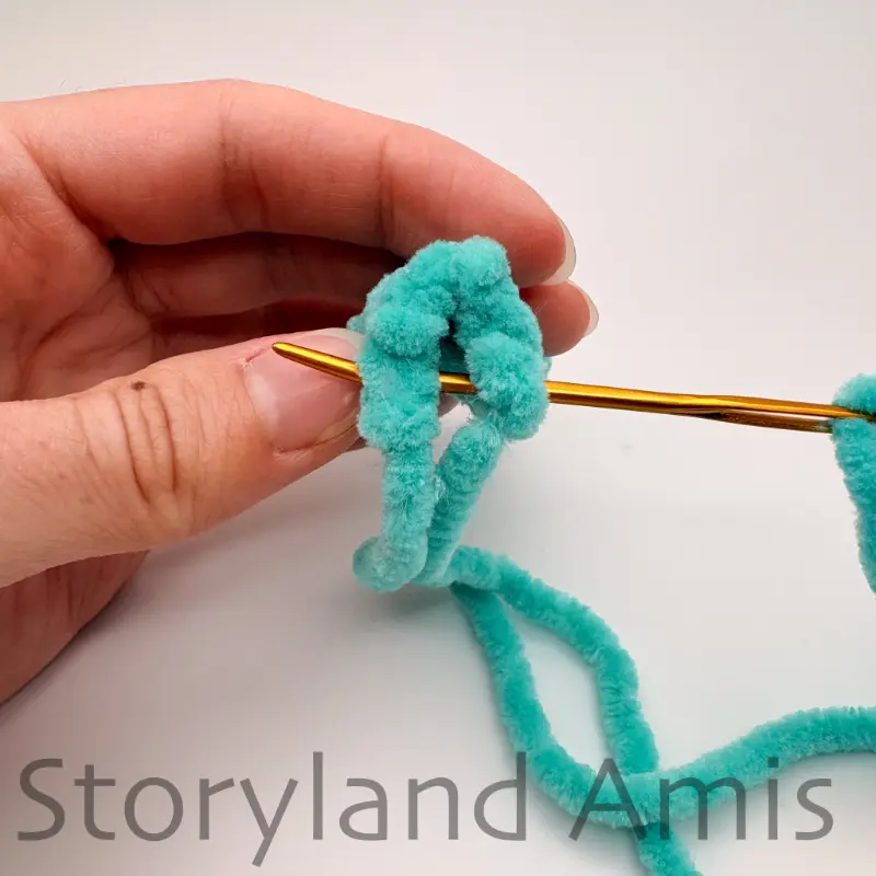 A hand holds a small, crocheted fish fin with a tapestry needle going through the top of it.