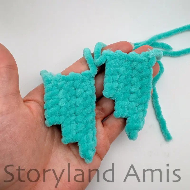 A hand holds two crocheted fish fins.
