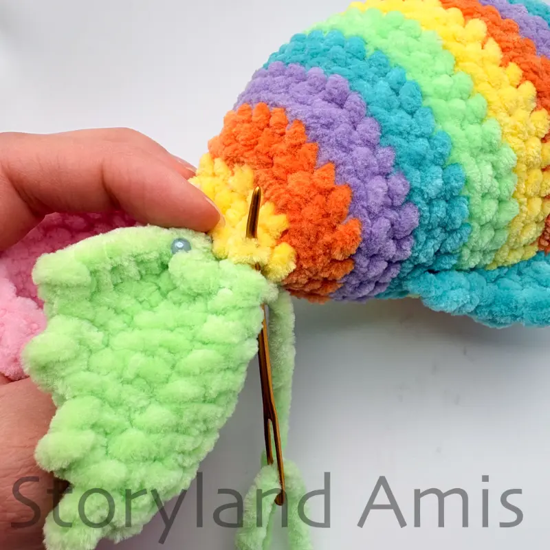 A close-up of a tapestry needle being used to sew a crocheted tail fin to the back of an amigurumi fish.