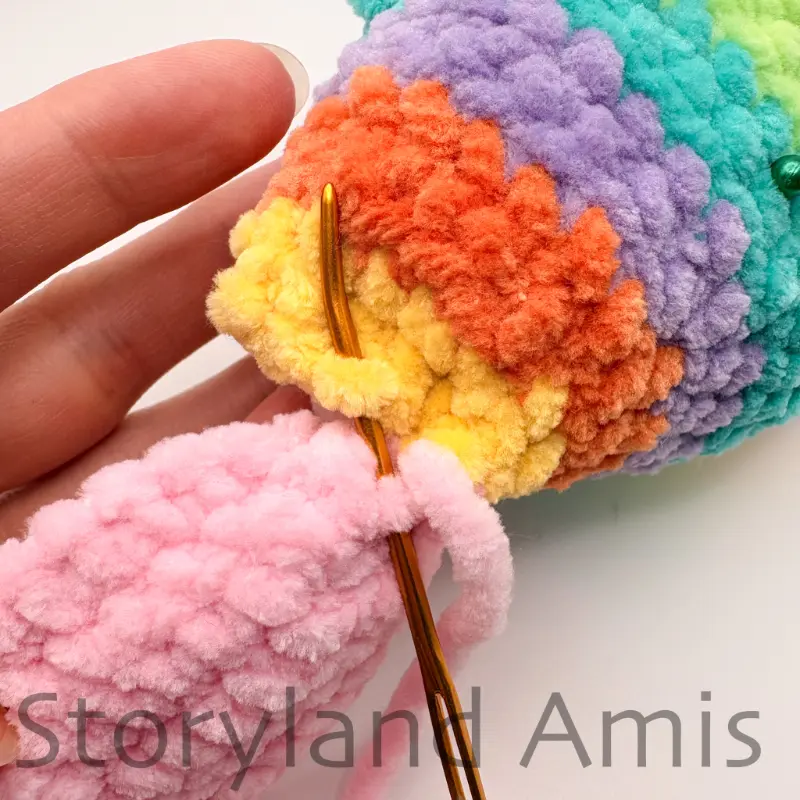 A close-up of a tapestry needle being used to sew a crocheted tail fin to the back of an amigurumi fish.