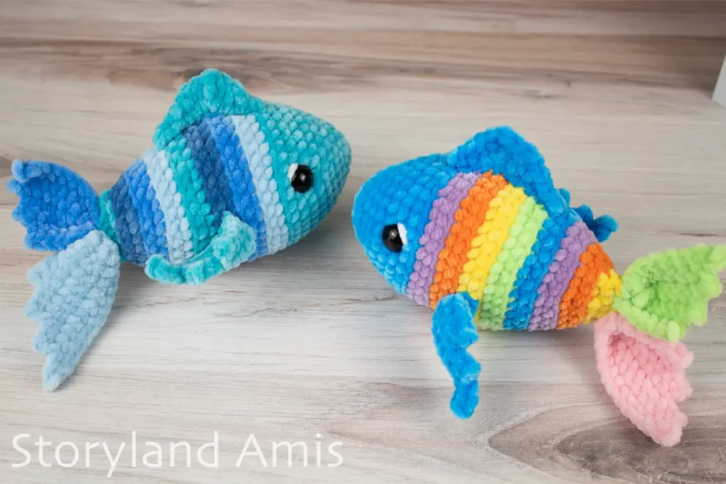 Two multicolored crocheted fish sit on a wooden table.