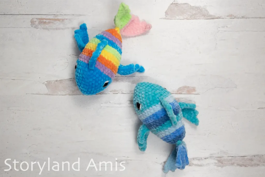 Two multicolored crocheted fish lay on a wooden table.