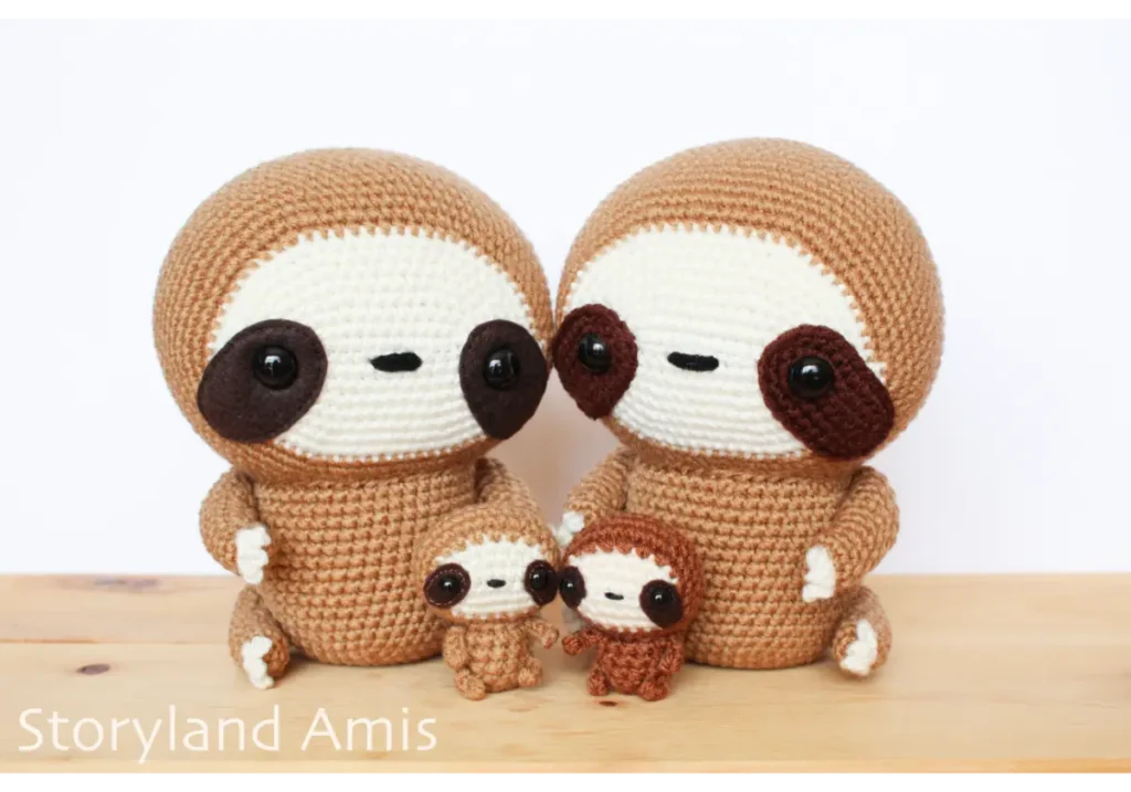 Four crocheted sloths sit on a wooden table.