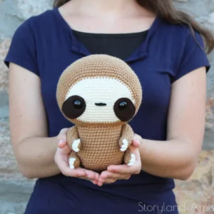 A girl holds a crocheted sloth toy.