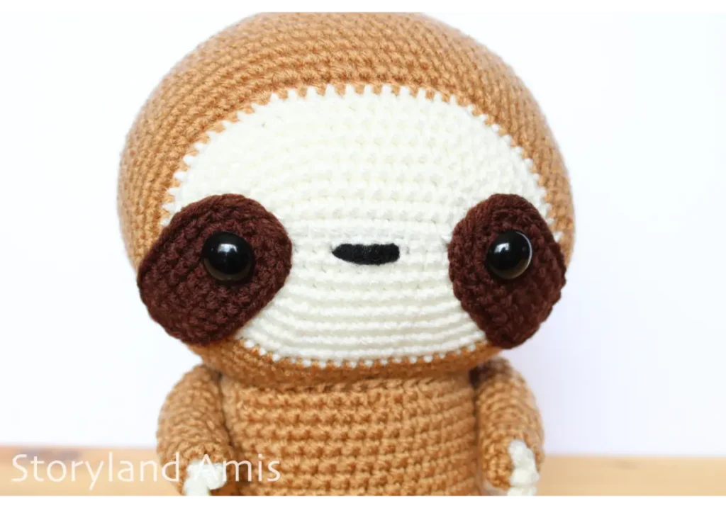 A close-up of the face of an amigurumi sloth toy.