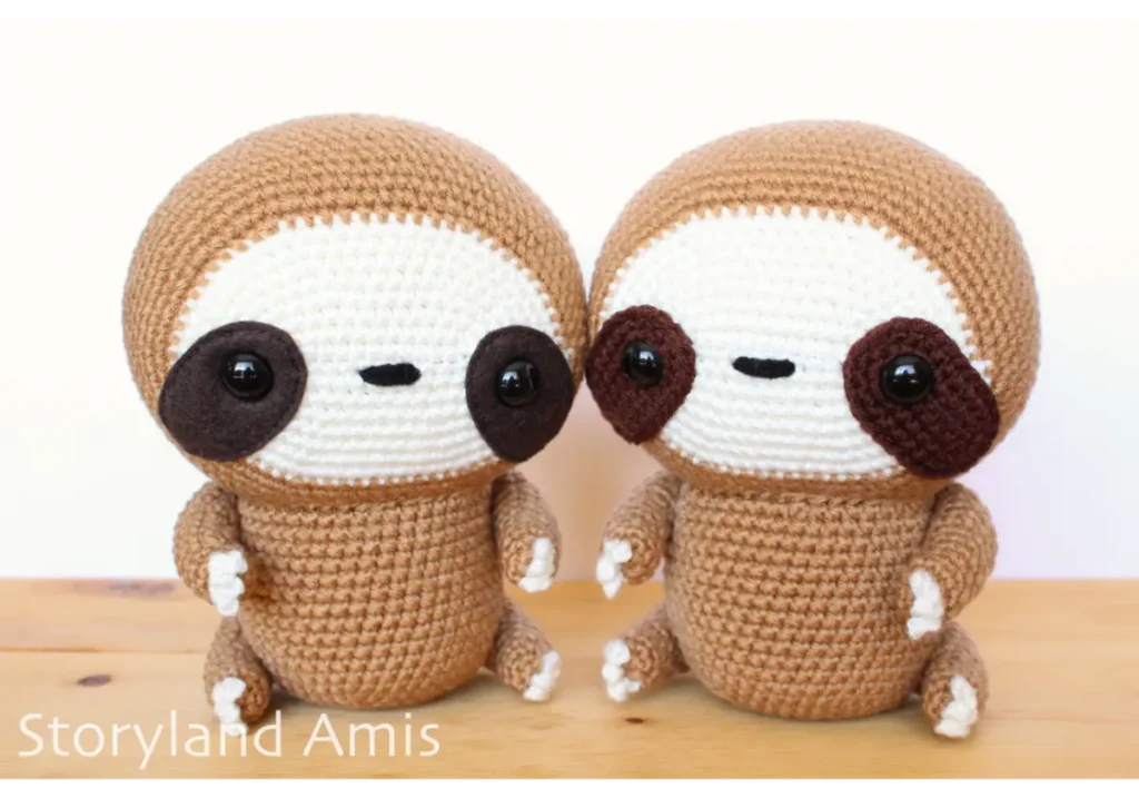 Two crocheted sloths sit together on a wooden table.