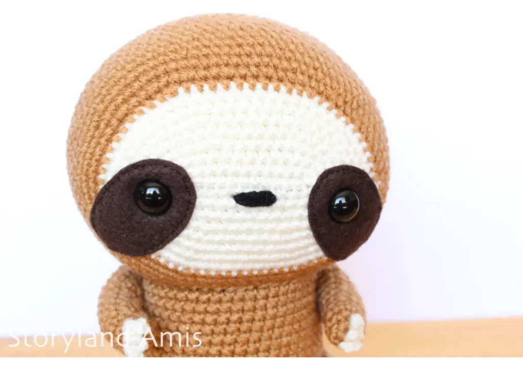 A close-up of the face of an amigurumi sloth toy.