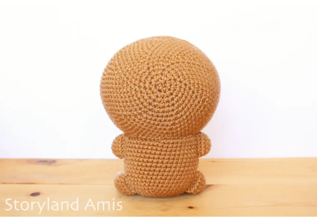 The backside of a crocheted amigurumi sloth sitting on a wooden table.