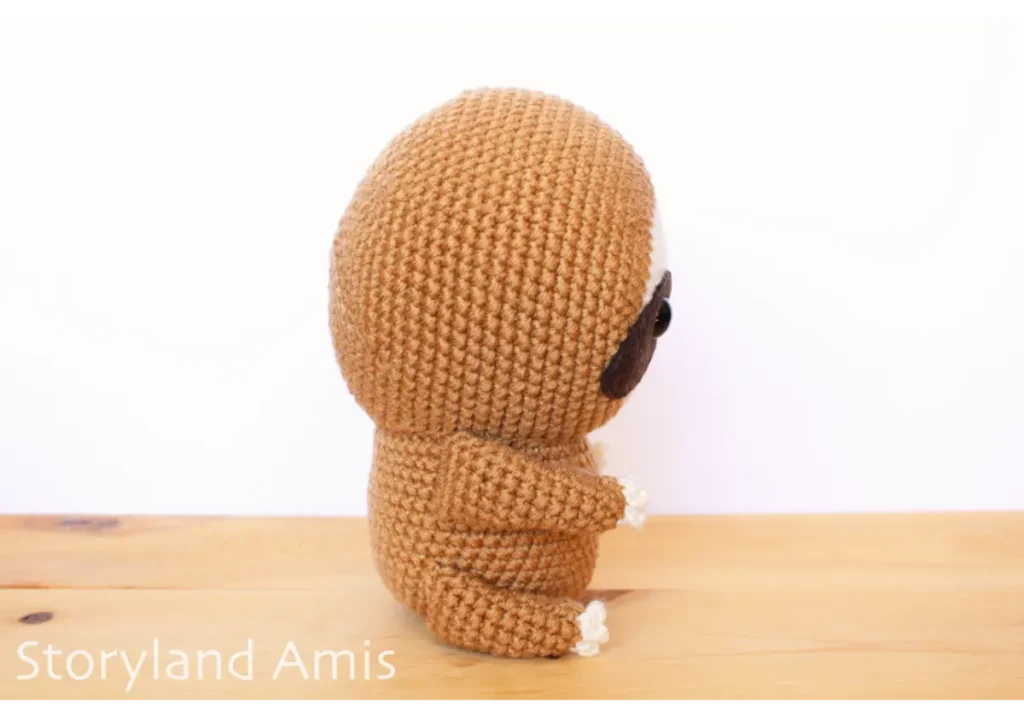 A crocheted amigurumi sloth sits on a wooden table.