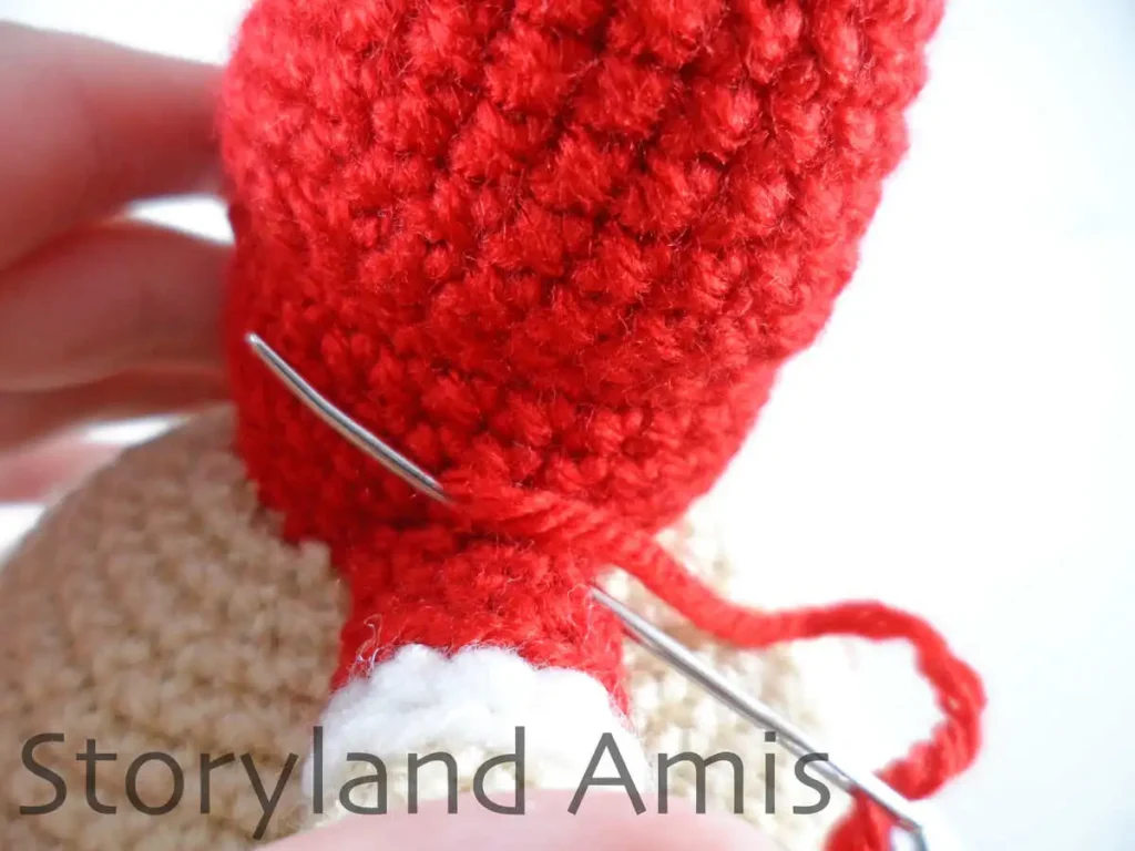 A close-up of a tapestry needle being used to sew a crocheted arm to the body of an amigurumi Mrs. Claus doll.