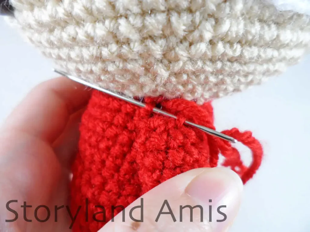 A close-up of a crocheted arm being sewing to the body of an amigurumi Mrs. Claus doll.