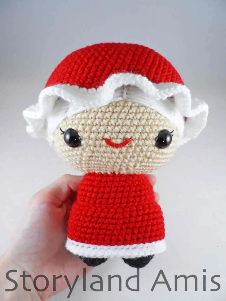 A hand holds a partially finished amigurumi Mrs. Claus doll.