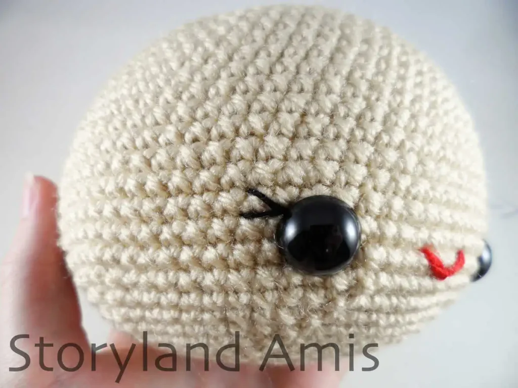 A close-up of a plastic safety eye on a crocheted amigurumi doll head.