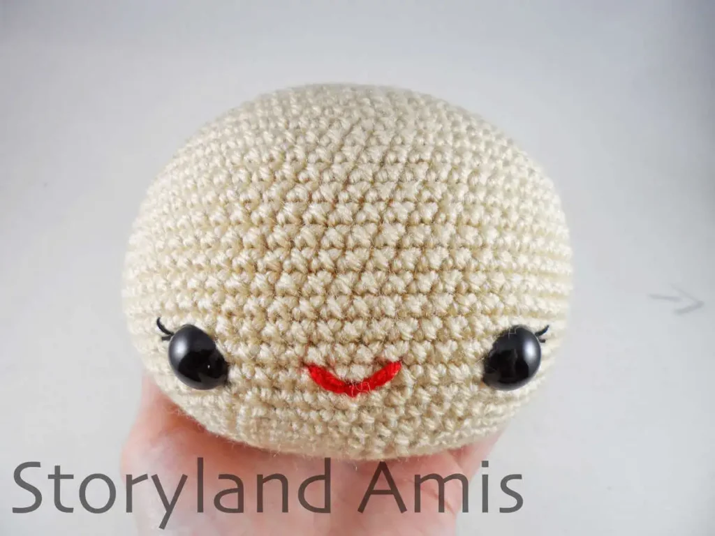 A hand holds a crocheted doll head.