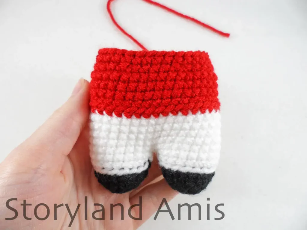 A hand holds a crocheted amigurumi Mrs. Claus body.