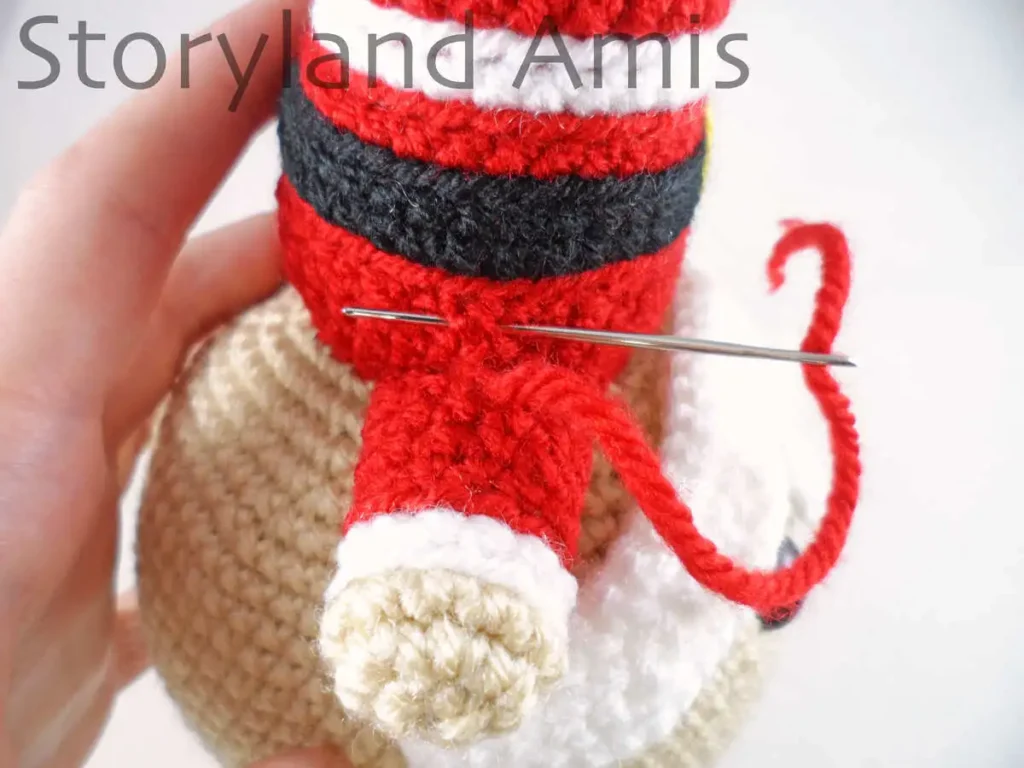 A close-up of a tapestry needle being used to sew a crocheted arm to the body of an amigurumi Santa Claus doll.