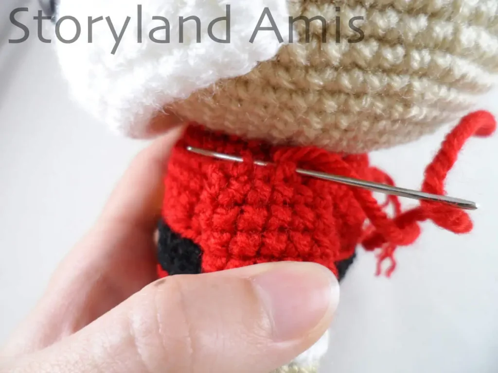 A close-up of a crocheted arm being sewing to the body of an amigurumi Santa Claus doll.