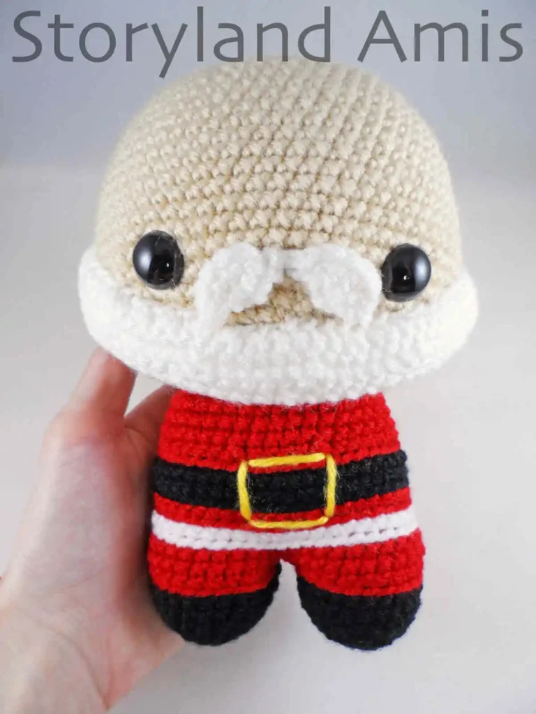 A hand holds a partially finished amigurumi Santa Claus doll.