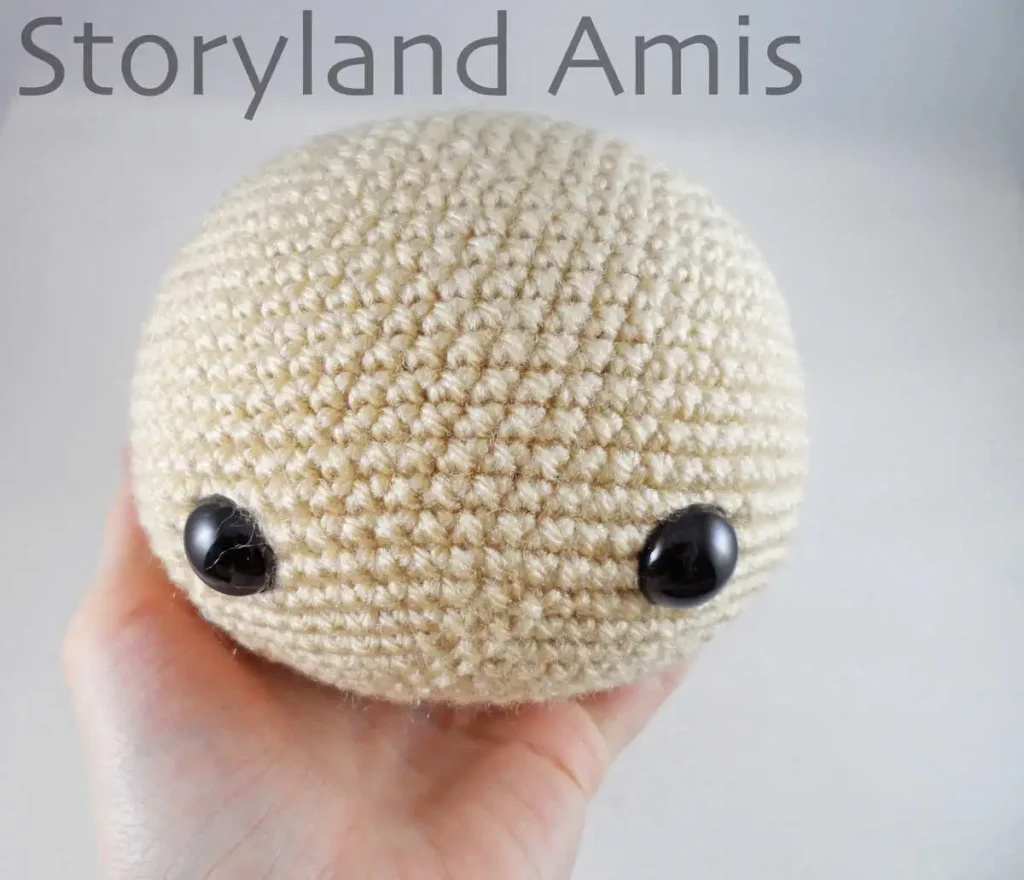 A hand holds a round crocheted doll head.